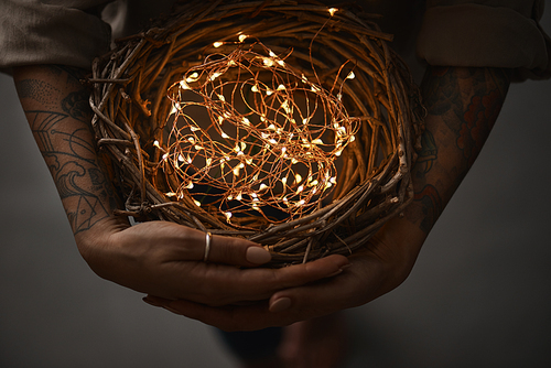 wreath of twigs and Christmas lights in female hands on a dark background flat lay