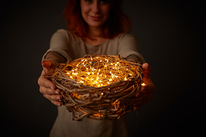 Happy girl with tattoo gives a festive wreath decorated with Christmas garlands around a black background. Holiday concept