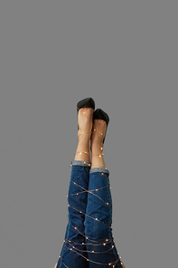 Slender legs of a woman in jeans with a garland around them on a gray background. Place for text.
