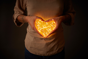 A woman holds the lights in the shape of a heart in the dark. The concept of the Valentine's Day