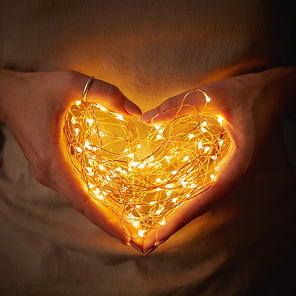 Close-up of lights in the shape of a heart, a woman holding in hands in the dark. The concept of a Valentine's Day