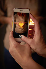 Woman takes pictures on the phone girl with christmas lights in the shape of heart
