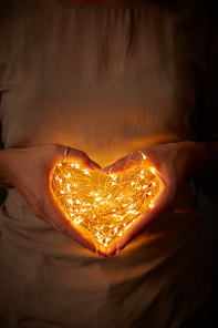 Yellow lights of a garland in the shape of a heart in female hands. St. Valentine's Day
