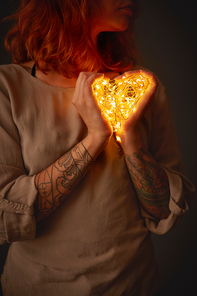 A young girl is holding yellow garland lights in the shape of a heart. St. Valentine's Day