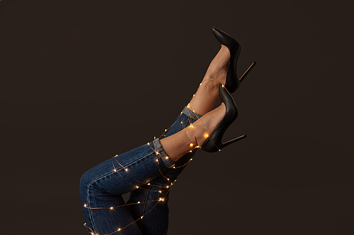 Legs of a woman in elegant black high-heeled shoes with bright christmas lights on a black background. As the layout for your ideas