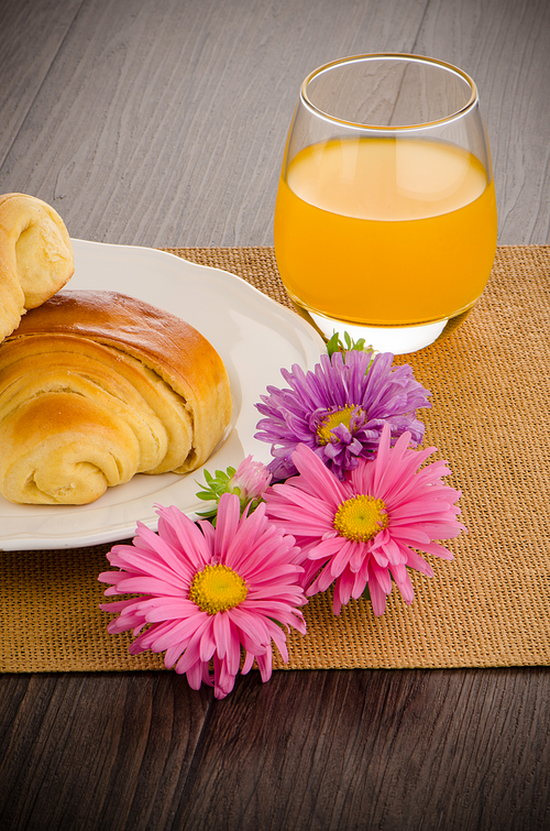 Closeup of croissants with orange juice with flowers on wooden table
