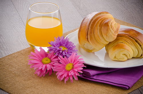 Closeup of croissants with orange juice with flowers on wooden table