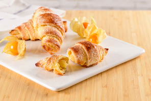 Small croissant with physalis fruits in white ceramic tray, homemade cakes on wooden table top.