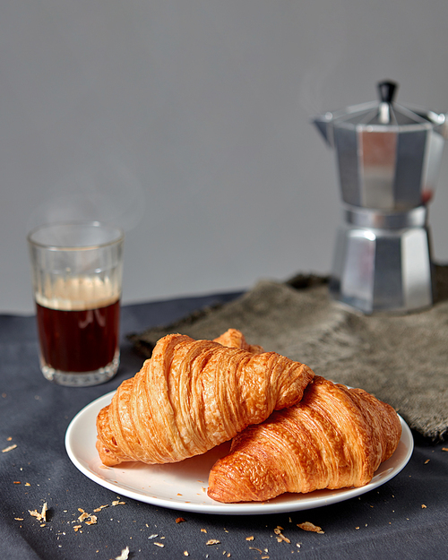 Freshly baked french pastry on a plate with glass of hot aromatic coffee and geyser maker on a dark texile background, copy space.