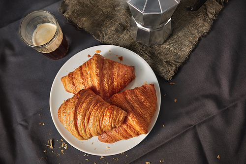 Top view of continental morning breakfast with homemade delicious french croissants on a plate and freshly brewed aromatic coffee on a dark textile, copy space.