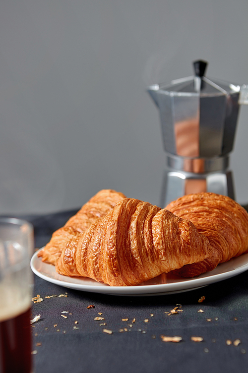 Italian coffee maker with morning hot aromatic beverage and homemade freshly baked french pastry on dark textile background. Place fo rtext. Continental breakfast.