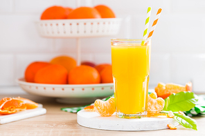 Tangerine orange juice in glass and fresh fruits with leaves on white wooden kitchen background closeup. Healthy and tasty refreshing summer beverage