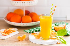 Tangerine orange juice in glass and fresh fruits with leaves on white wooden kitchen background closeup. Healthy and tasty refreshing summer beverage