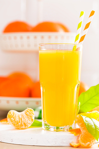 Tangerine orange juice in glass and fresh fruits with leaves on white wooden kitchen background closeup. Healthy and tasty refreshing summer beverage