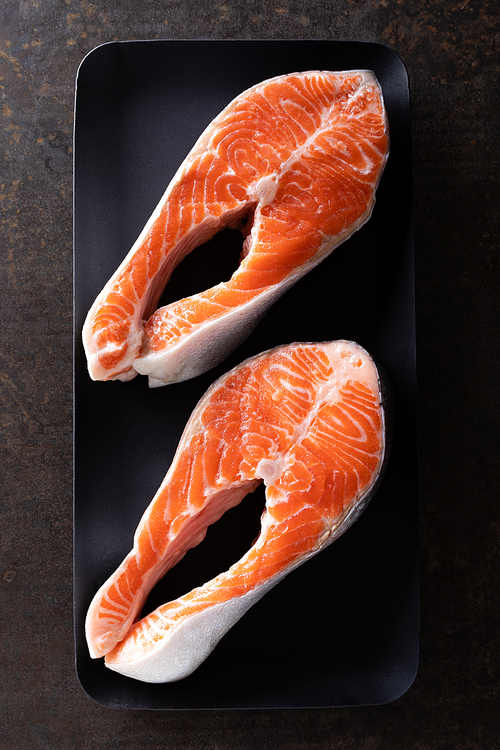 Fresh salmon fish steaks on black background top view