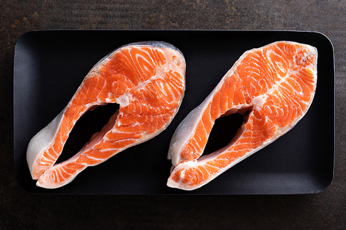 Fresh salmon fish steaks on black background top view