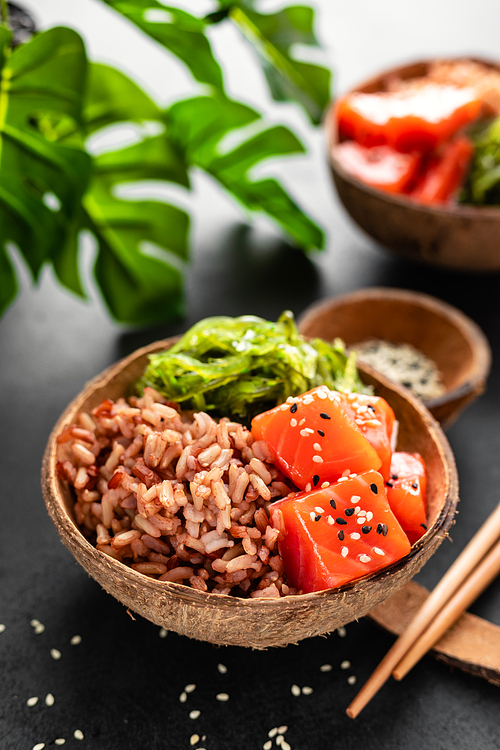 poke bowl with raw salmon fish, chuka salad and food in coconut bowls on black background