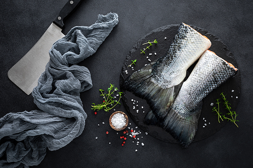 Raw salmon fishtails with ingredients for cooking on black background, top view