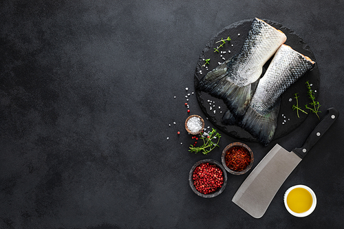 Raw salmon fishtails with ingredients for cooking on black background, top view