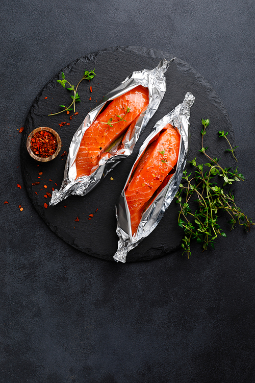 Raw salmon fish fillet in foil on black background