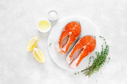 Fresh salmon steaks with ingredients for cooking on white board, view from above