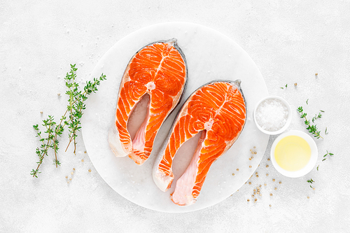 Fresh salmon steaks with ingredients for cooking on white board, view from above