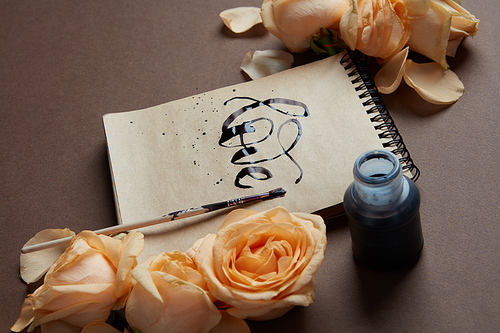Diary or notebook with word love written with help of ink. Diary covered by flowers roses against brown background. Valentine's Day concept.