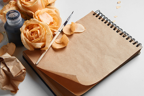 Closeup of diary or notebook covered by orange roses and their flowers for your notes. Ink pen is nice idea for representing your ideas and emotions on brown pages.