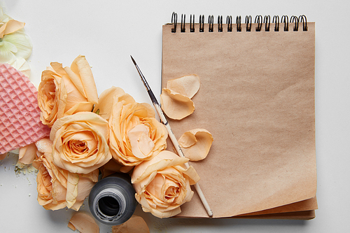 Valentine's Day concept. Ink pen is nice idea for representing your ideas and emotions on brown pages. Closeup of diary or notebook covered by orange roses and their flowers for your notes.
