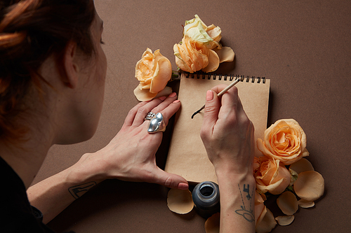 Woman with brush writing on paper with roses buds