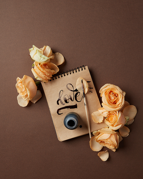 Notepad with written word Love and flowers on a brown background, flat lay