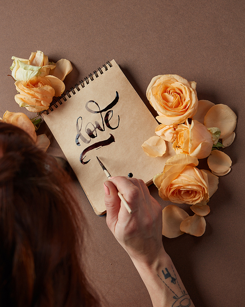 Back view of young woman writing love word with brush. Decorated with flowers