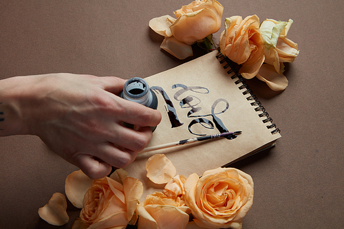 Female hand writing love word on craft paper, roses around