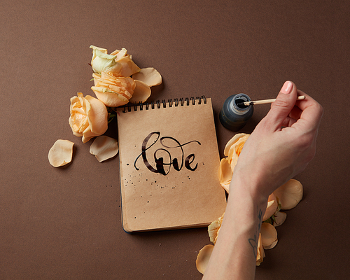 Valentine's Day concept. Diary or notebook with word love written by female. Female's hand writing in diary with brown pages over brown background.