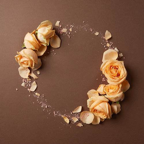 round frame of beige roses on a brown background, flat lay