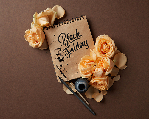 Notepad with a caligraphic text and a frame of flowers on a brown background, Sale concept Black Friday flat lay copy space