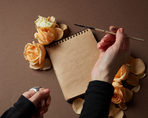 Female's hand holding pen over diary or notebook for making notes concerning Valentine's Day. Notebook covered by orange roses. Valentine's Day concept.