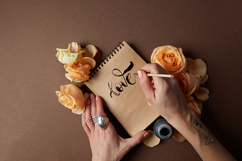 Female's hand writing word love in diary or notebook with ink. Word corresponding to Valentine's Day. Diary is covered by beautiful orange flowers.