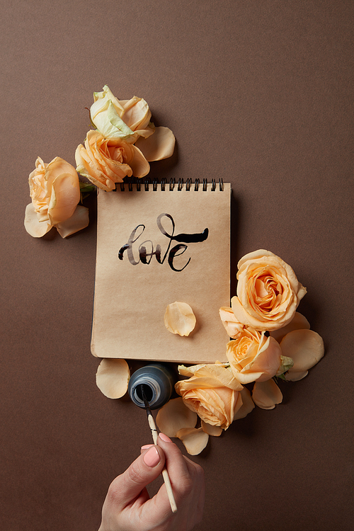 Female hands writing down on letter paper for Valentine's day with flowers on a brown background