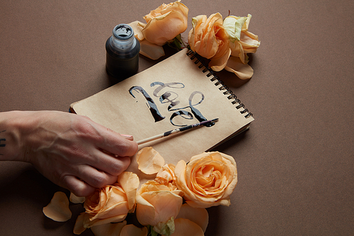 girl writing the word Love in a notebook on a brown background with flowers.