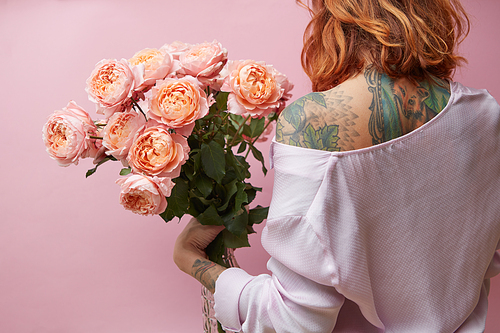 Girl with a tattoo on her back holds a big bouquet of pink roses media on a pink background,view from the back. Valentine's Day, Mother's Day