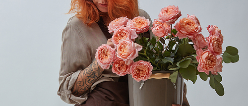 Fresh bouquet of roses in a vase. A red-haired woman with a tattoo on her arm is holding a vase with pink roses. Mothers Day.