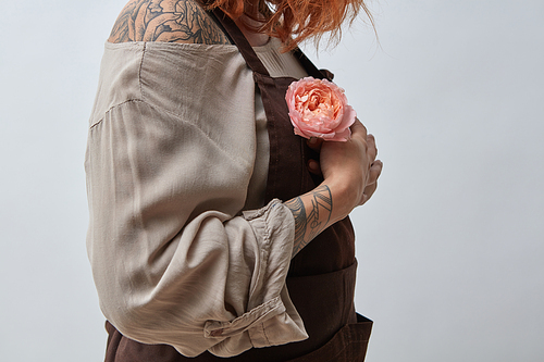 A girl with a tattoo and in an apron holds in her hand a pink flower Ranunculus on a gray background. Mother's Day, Valentine's Day