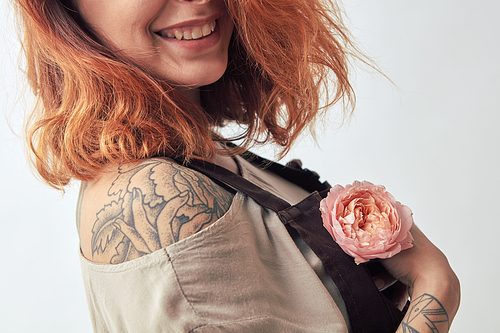 Smiling girl with a tattoo holds in her hand a pink flower Rununculus on a gray background. Mother's Day, Valentine's Day