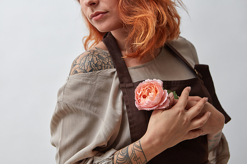 Red-haired girl with a tattoo holds in her hand a pink flower of a Ranunculus on a gray background. Mother's Day, Valentine's Day