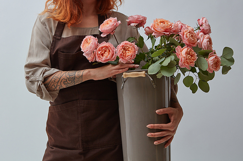 A woman with a tattoo is holding a big vase with pink media roses. Mothers Day. Flowers shop concept