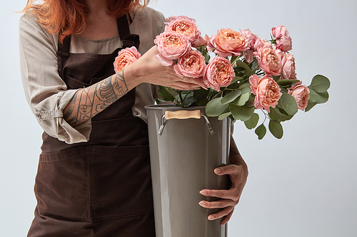 A woman in a brown apron holds a vase with fresh pink roses. Flowers shop concept