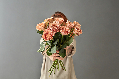 A woman gives a bouquet of beige roses cappuccino, on a gray background. Mother's Day,