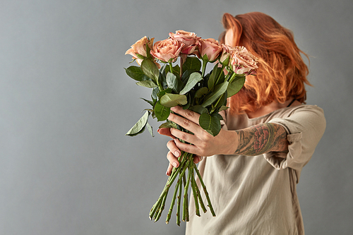 Red-haired girl gives a bouquet of beige roses cappuccino, on a gray background. Mother's Day,