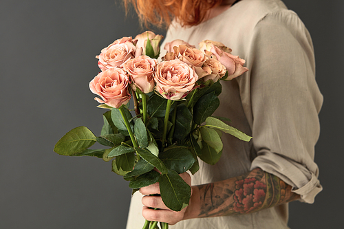 Girl with a tattoo holds a bouquet of fresh pink roses on a gray background. Happy valentine's day. Happy Mother's Day
